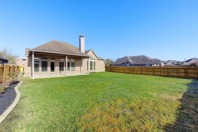 rear view of property with brick siding, a patio area, a fenced backyard, and a lawn