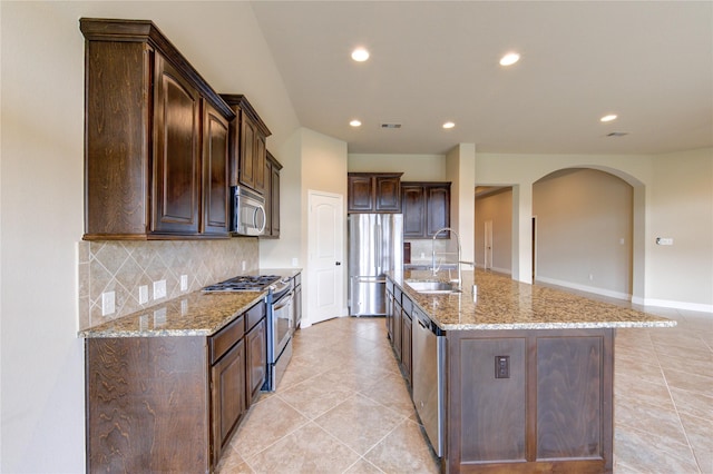 kitchen featuring a sink, backsplash, stainless steel appliances, arched walkways, and dark brown cabinetry