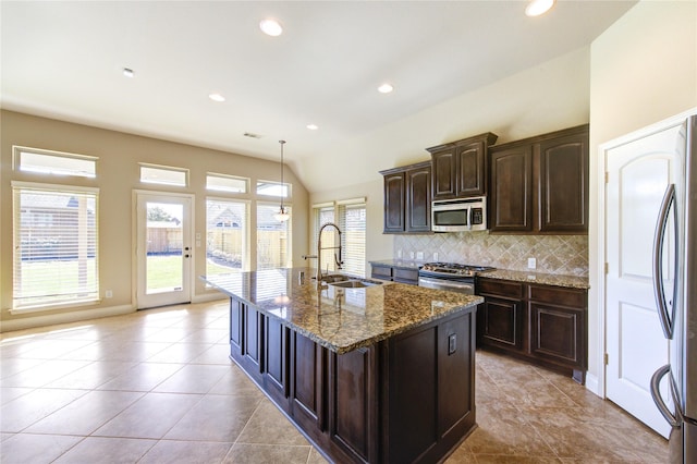 kitchen featuring a center island with sink, a sink, dark stone countertops, tasteful backsplash, and stainless steel appliances