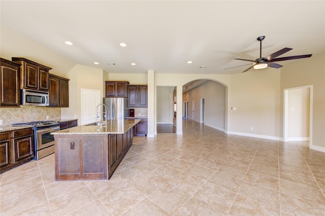 kitchen with arched walkways, a sink, decorative backsplash, stainless steel appliances, and open floor plan