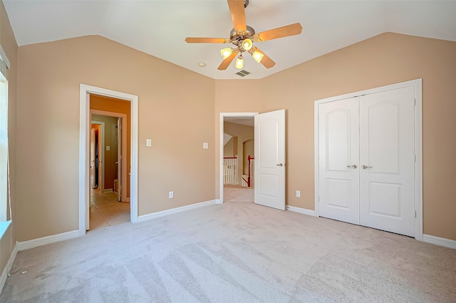 unfurnished bedroom with baseboards, visible vents, lofted ceiling, a closet, and light carpet