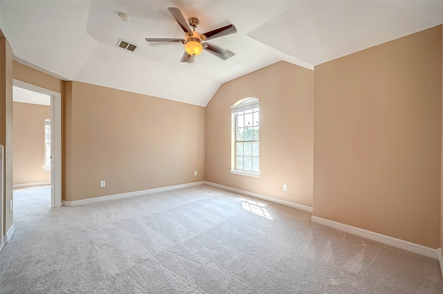 spare room featuring visible vents, light carpet, baseboards, ceiling fan, and vaulted ceiling