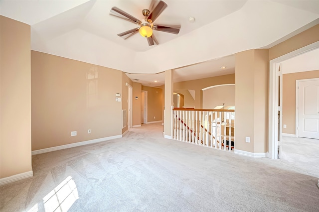 carpeted spare room featuring a tray ceiling, baseboards, arched walkways, and ceiling fan