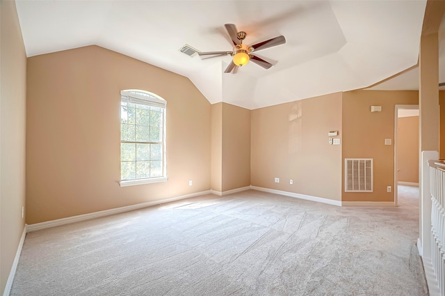 spare room featuring light colored carpet, lofted ceiling, a ceiling fan, and visible vents