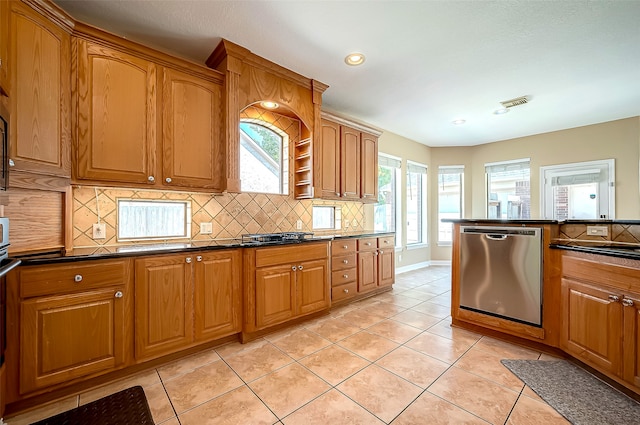 kitchen featuring stainless steel dishwasher, dark countertops, light tile patterned flooring, brown cabinetry, and decorative backsplash