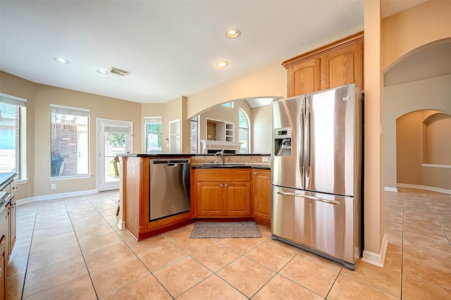 kitchen featuring dark countertops, recessed lighting, stainless steel appliances, arched walkways, and light tile patterned floors