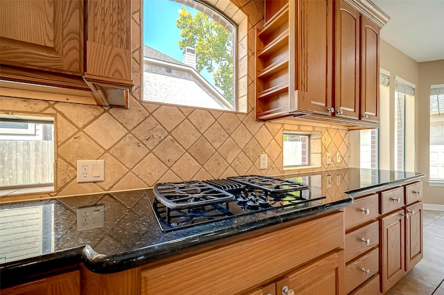 kitchen with black gas cooktop, dark stone counters, light tile patterned floors, decorative backsplash, and plenty of natural light