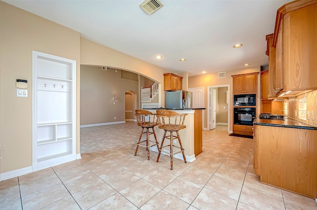 kitchen with visible vents, a breakfast bar, arched walkways, black appliances, and dark countertops