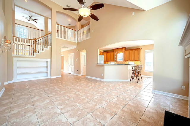 unfurnished living room with ceiling fan, arched walkways, light tile patterned flooring, baseboards, and a towering ceiling