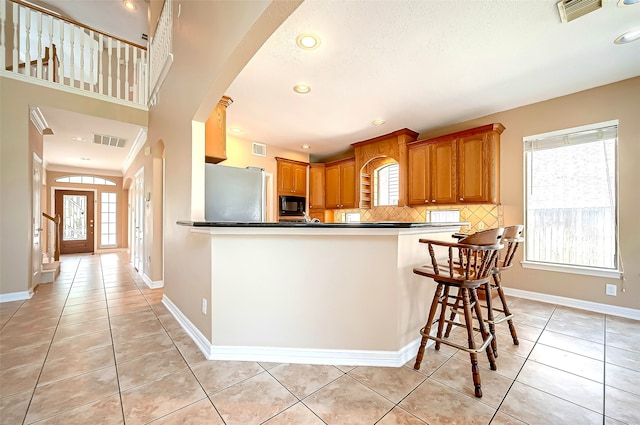 kitchen featuring freestanding refrigerator, light tile patterned floors, visible vents, and black microwave