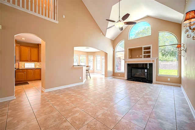 unfurnished living room with light tile patterned flooring, arched walkways, a tile fireplace, and ceiling fan