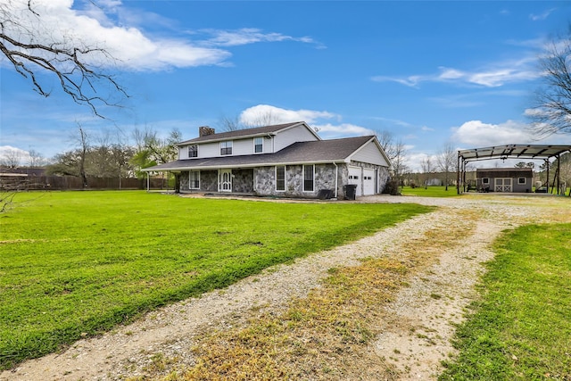 back of house featuring a detached carport, a chimney, a garage, a yard, and driveway