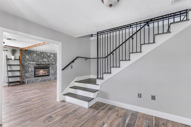 staircase with a fireplace, wood finished floors, visible vents, and baseboards