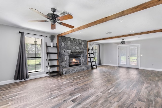 unfurnished living room featuring visible vents, beamed ceiling, a stone fireplace, wood finished floors, and a ceiling fan