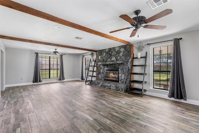 unfurnished living room with visible vents, wood finished floors, a stone fireplace, and ceiling fan