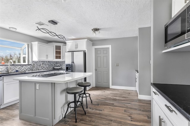 kitchen featuring glass insert cabinets, a breakfast bar, dark wood-style flooring, appliances with stainless steel finishes, and a sink