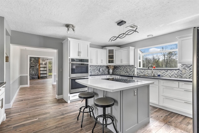 kitchen with wood finished floors, stainless steel double oven, a sink, black electric cooktop, and tasteful backsplash