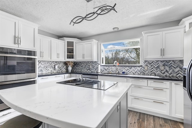 kitchen with black electric stovetop, dark wood-style floors, stainless steel double oven, white cabinetry, and a sink