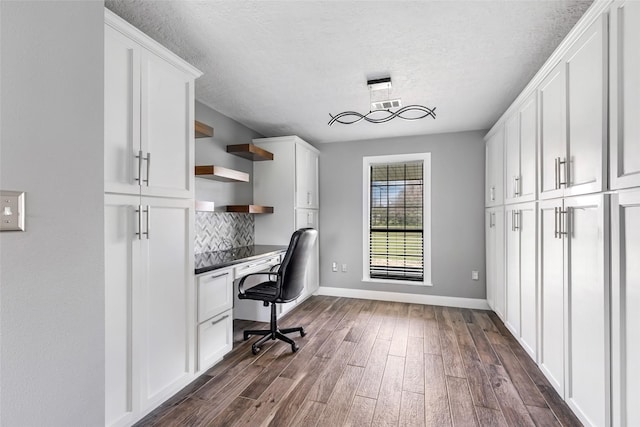 unfurnished office featuring visible vents, dark wood-type flooring, built in desk, and a textured ceiling