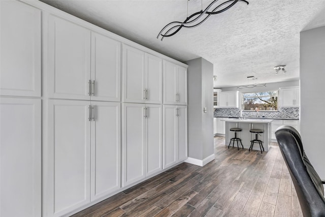 kitchen featuring dark wood-type flooring, white cabinetry, tasteful backsplash, a kitchen bar, and a center island