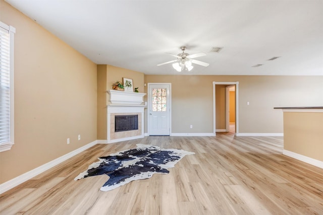 unfurnished living room featuring visible vents, baseboards, ceiling fan, a tile fireplace, and wood finished floors