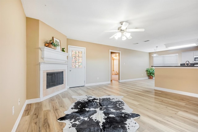 living room featuring baseboards, ceiling fan, a fireplace, and light wood finished floors