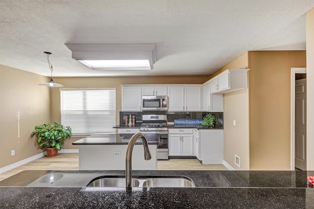 kitchen with decorative light fixtures, light wood-type flooring, appliances with stainless steel finishes, and white cabinetry