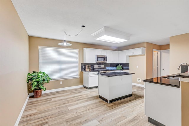 kitchen featuring a sink, a kitchen island, dark countertops, stainless steel appliances, and white cabinets