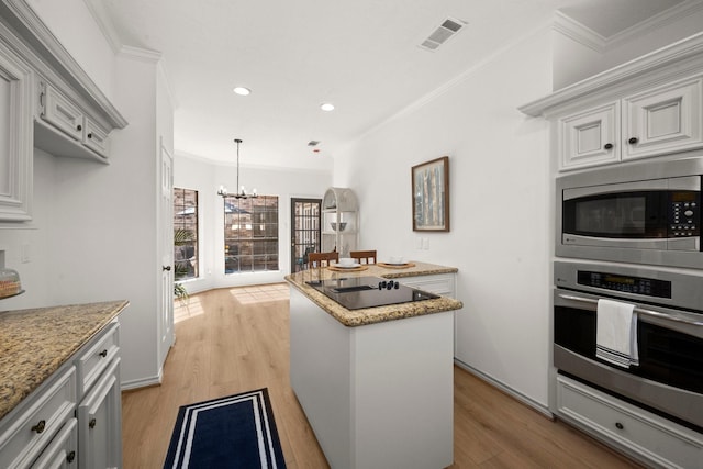 kitchen featuring visible vents, a kitchen island, appliances with stainless steel finishes, crown molding, and a chandelier