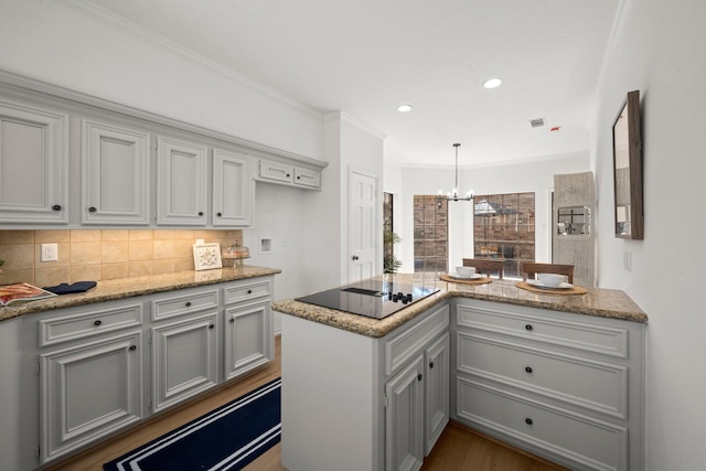 kitchen featuring wood finished floors, ornamental molding, a notable chandelier, black electric cooktop, and backsplash