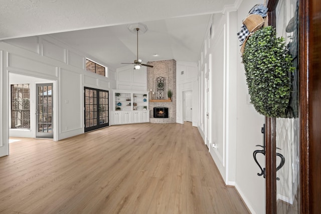 unfurnished living room with light wood-style flooring, a ceiling fan, built in features, a fireplace, and a decorative wall