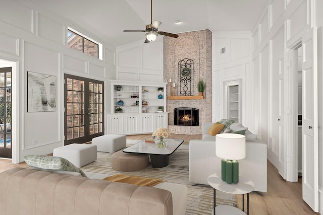 living room with built in shelves, a fireplace, a decorative wall, high vaulted ceiling, and a ceiling fan