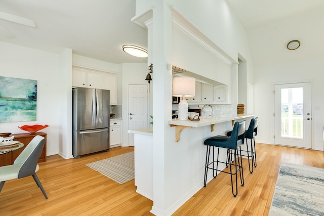 4010 Kiva Rd, Galveston, TX 77554 - kitchen with freestanding refrigerator, decorative backsplash, light wood-style flooring, and a kitchen breakfast bar