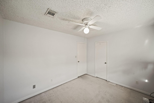 unfurnished room featuring visible vents, light colored carpet, a textured ceiling, and ceiling fan