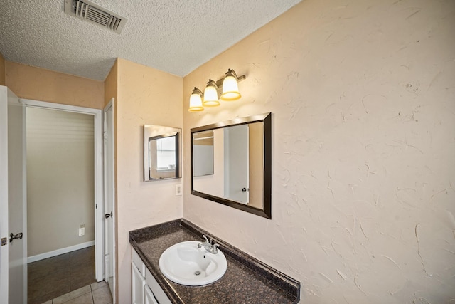 bathroom with vanity, visible vents, tile patterned flooring, a textured ceiling, and a textured wall