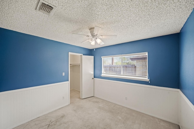 unfurnished bedroom featuring visible vents, wainscoting, and a textured ceiling