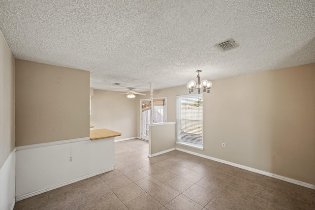 empty room with tile patterned flooring, visible vents, baseboards, ceiling fan with notable chandelier, and a textured ceiling