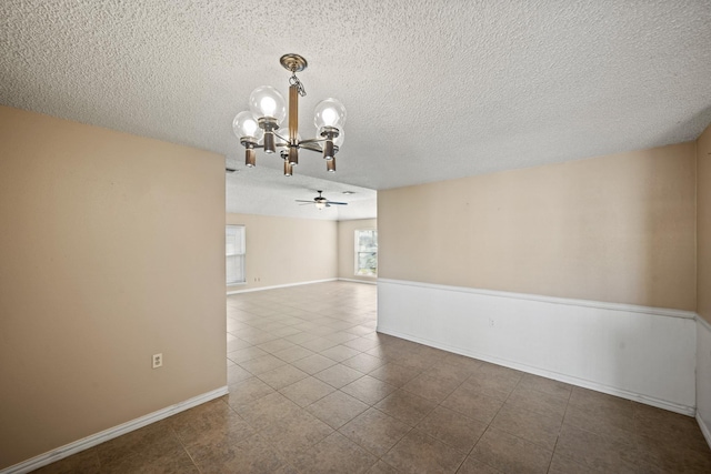 tiled spare room featuring baseboards, a textured ceiling, and ceiling fan with notable chandelier