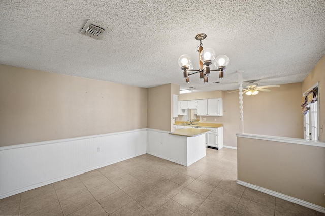 unfurnished room with visible vents, ceiling fan with notable chandelier, a sink, a textured ceiling, and wainscoting