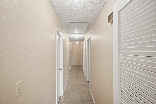 hallway with light tile patterned floors, visible vents, baseboards, attic access, and a textured ceiling