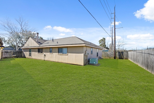 rear view of property with central air condition unit, a lawn, roof with shingles, and a fenced backyard