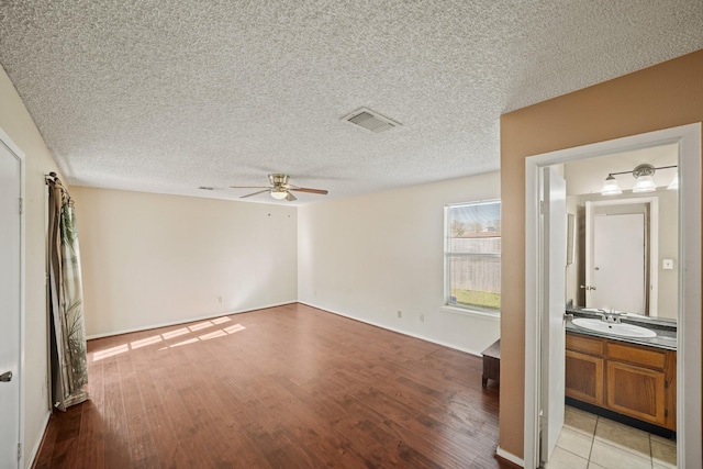 unfurnished bedroom featuring visible vents, light wood-style flooring, a textured ceiling, a ceiling fan, and a sink