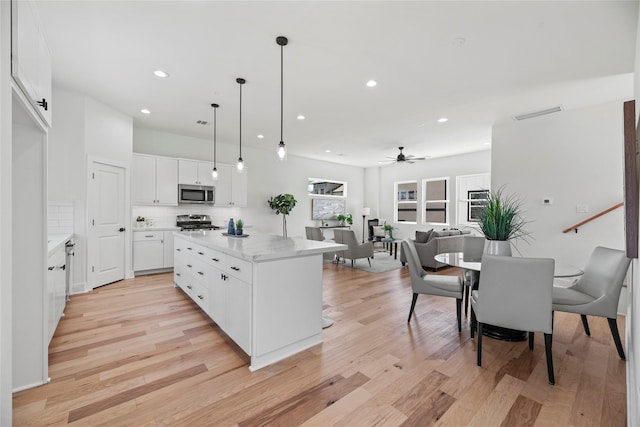 kitchen featuring backsplash, a kitchen island, light wood-type flooring, stainless steel appliances, and a ceiling fan