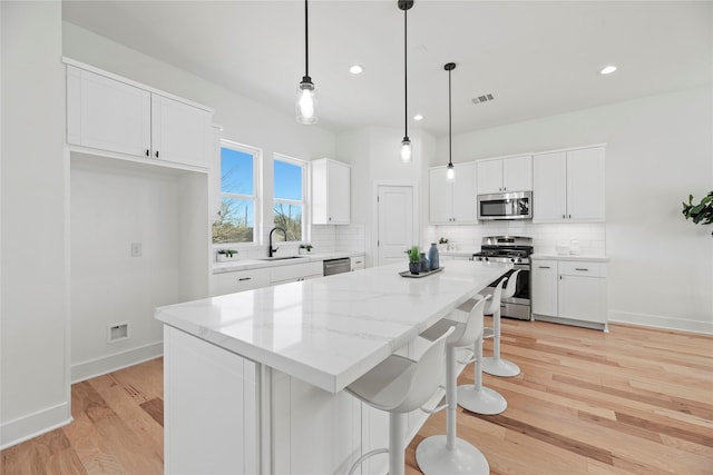 kitchen with decorative backsplash, white cabinets, appliances with stainless steel finishes, and a kitchen island