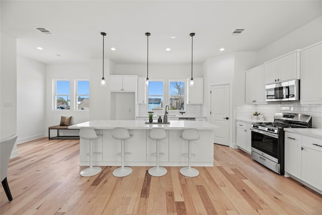 kitchen with visible vents, backsplash, light wood-type flooring, light countertops, and appliances with stainless steel finishes