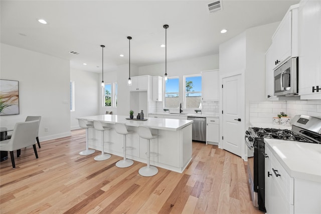 kitchen with visible vents, a breakfast bar, light wood-type flooring, appliances with stainless steel finishes, and a sink