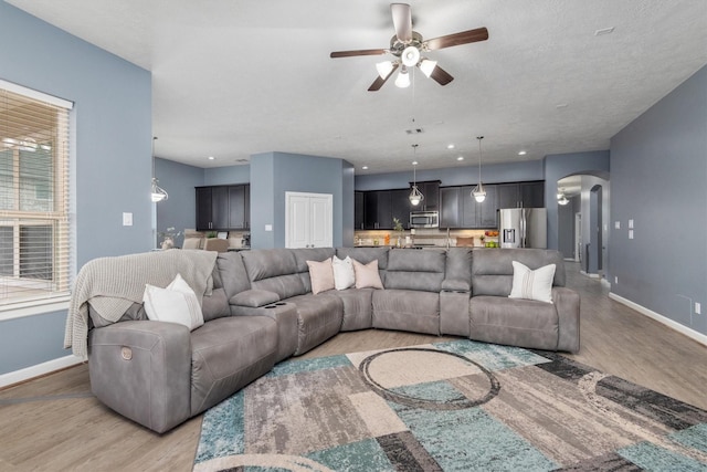 living area featuring light wood-style floors, a ceiling fan, arched walkways, and baseboards