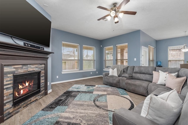 living room featuring baseboards, a stone fireplace, wood finished floors, and a ceiling fan