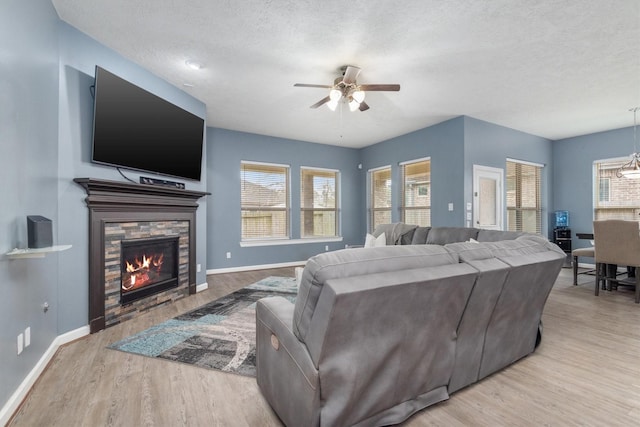 living room with ceiling fan with notable chandelier, a fireplace, a textured ceiling, and wood finished floors