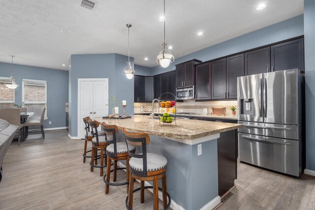 kitchen featuring light wood-type flooring, visible vents, light stone counters, appliances with stainless steel finishes, and decorative backsplash